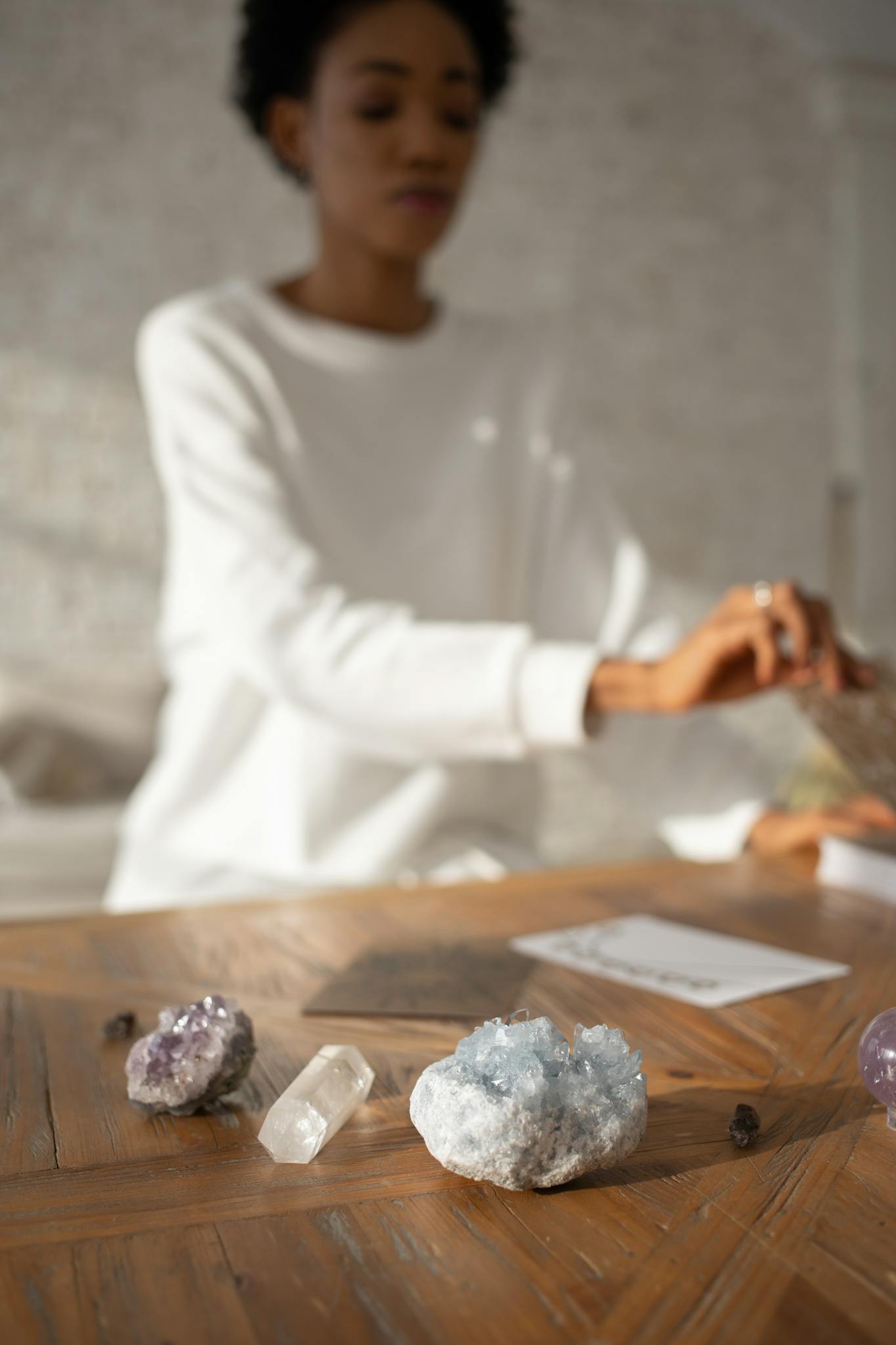 A woman arranges crystals on a wooden table in a well-lit indoor setting.